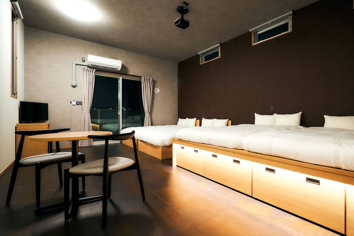 A hotel room with a bed, bedside tables, a chair, and an air conditioning unit.