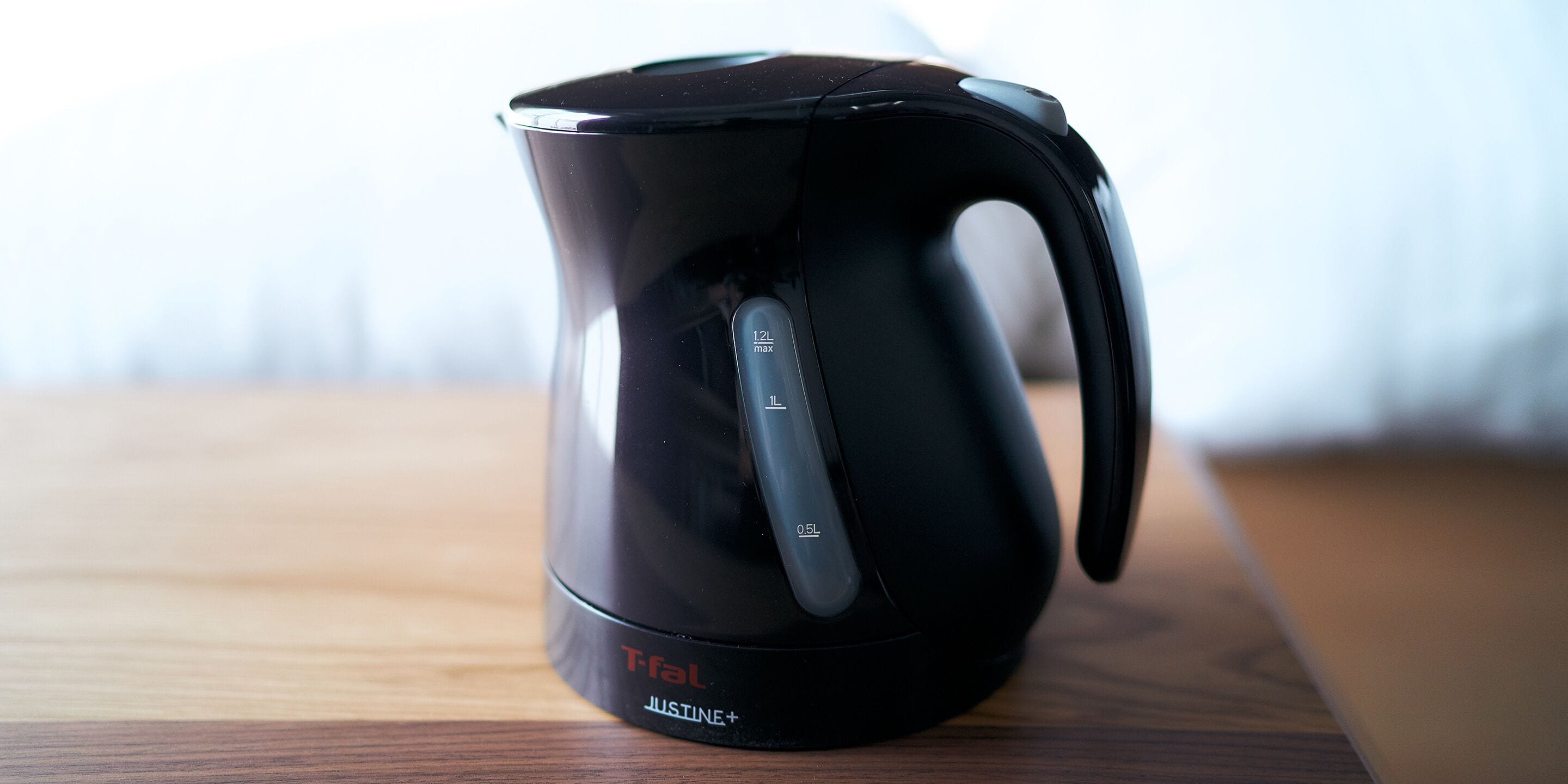A black electric kettle with a handle and a spout, placed on a wooden surface.