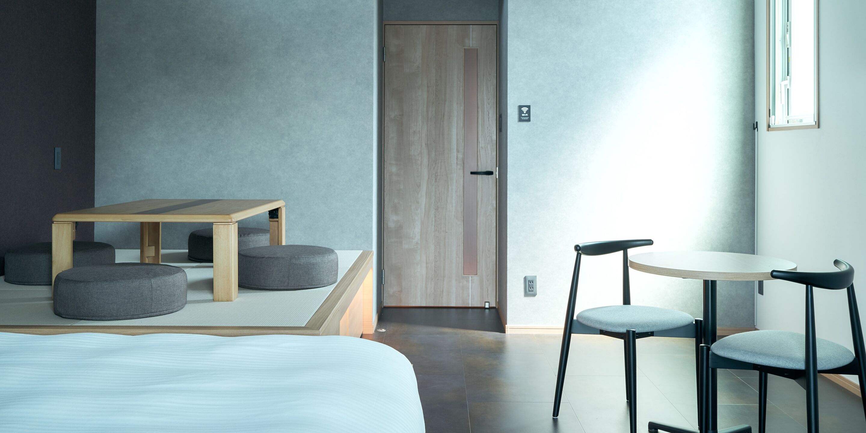 A modern hotel room with a bed, a small wooden table, two chairs, and a sofa.