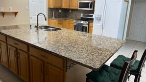 A kitchen with granite countertops, wooden cabinets, a stainless steel sink, a microwave, a stove, and a refrigerator.