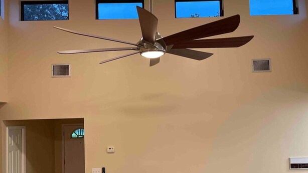 A ceiling fan in a room with high ceilings, two windows, and a door.