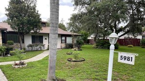 A residential property with a well-maintained lawn, a palm tree, and a street sign with the number 5981.
