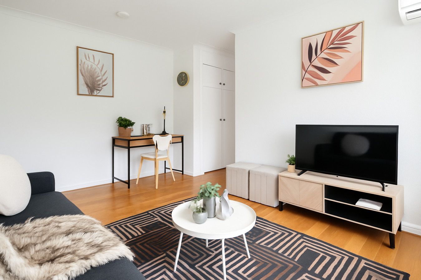 Una sala de estar moderna con un sofá, una mesa de centro, un televisor, un escritorio y un armario.