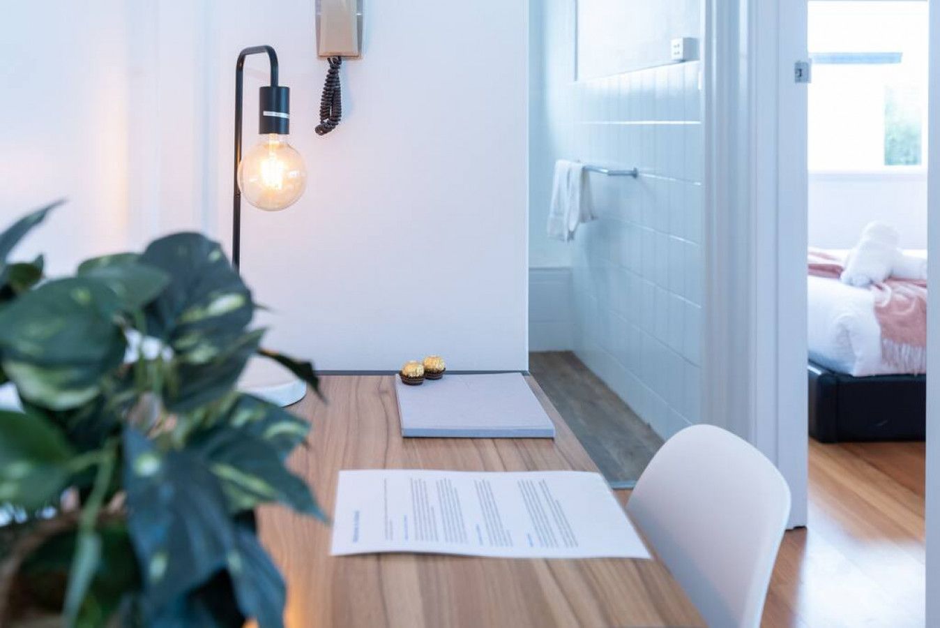 Ein modernes Zimmer mit Holzboden, einem Schreibtisch mit Pflanze, einer Lampe und einem Bett mit Blick.