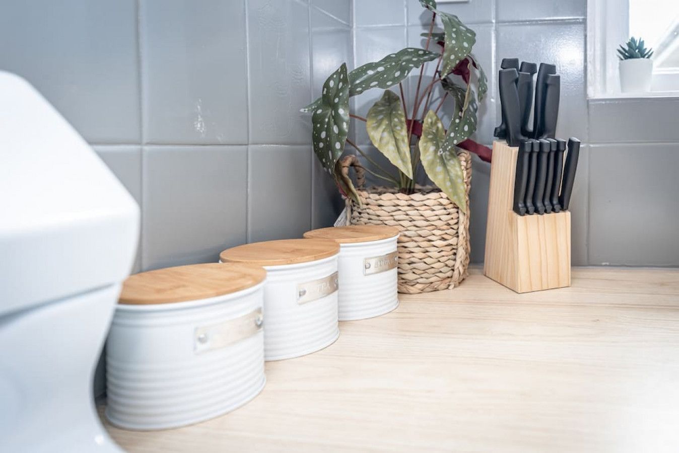 A kitchen with white storage bins, a woven basket with a plant, and a knife block.