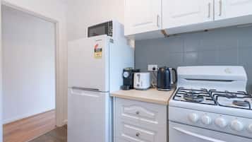 A compact kitchen with a refrigerator, a toaster, a kettle, and a stove.