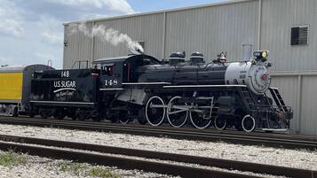 Una locomotora de vapor con el número 148 y el texto "U.S. Sugar" en su lateral, circulando sobre vías con lecho de grava.