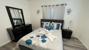 A bedroom with a bed, a dresser, a nightstand, a mirror, and a window with curtains.
