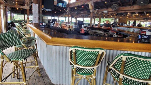 A bar area with wooden beams, green checkered chairs, and a counter with various bottles and a Budweiser sign.