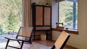 Una habitación con dos sillas de mimbre, un mueble de madera con plantas y una máquina de coser sobre un alféizar.