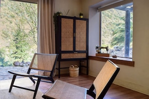 A room with two wicker chairs, a wooden cabinet with plants, and a sewing machine on a windowsill.