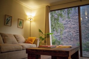 Relax in this serene space with a comfortable sofa, coffee table, and floor lamp, offering a peaceful view of the surrounding landscape.