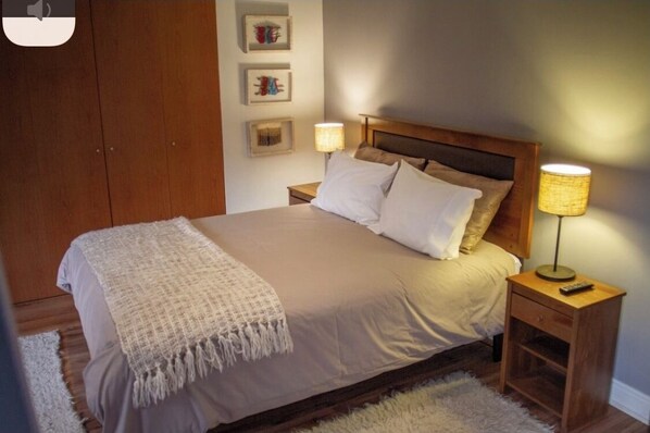 A neatly made bed with a wooden headboard, a bedside lamp, and a small bedside table with a remote control. - House on the way to Farellones (Santiago)