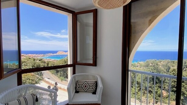 A balcony with a view of the sea, a wicker chair, a white sofa, and a hanging light fixture. - Residence La Listrella apt 4 (Monticello)