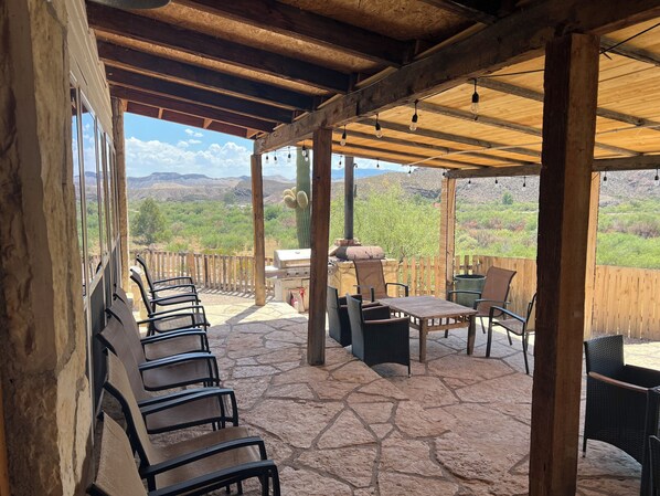 An outdoor patio with stone flooring, wooden furniture, and a view of the desert landscape.