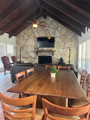 A spacious dining area with a large wooden table, surrounded by wooden chairs, under a vaulted ceiling with exposed beams.