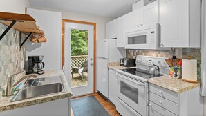 Una cocina compacta con armarios blancos, un lavamanos de acero inoxidable, un microondas, un horno y un tostador.