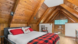 Un dormitorio con techo de madera, una cama con ropa de cama roja y blanca, una manta a cuadros y una silla.