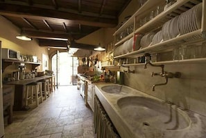 A kitchen with a large sink, shelves with dishes, and a view into another room.
