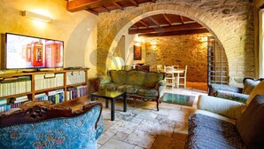 Un salon chaleureux avec une arche en pierre, des poutres en bois, un téléviseur, des étagères à livres et des sièges confortables.