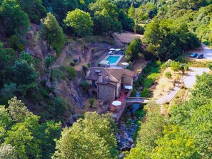 An aerial view of a villa with a swimming pool, stone architecture, and a surrounding natural landscape.