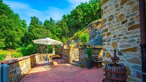 Une terrasse en pierre avec une table et des chaises, un tonneau en bois et un mur en pierre rustique.