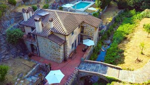 Une maison en pierre avec une piscine, un espace extérieur aménagé et un pont enjambant un ruisseau.
