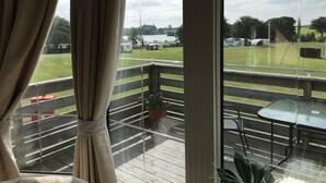 Ein Balkon mit Blick auf ein Wiesenfeld und abgestellte Wohnwagen.