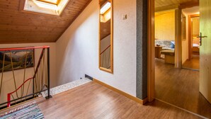 Une pièce avec un plancher en bois, une lucarne, un miroir et une porte donnant sur une autre pièce.