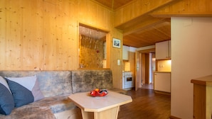 L’intérieur d’une cabane en bois, avec un banc en bois, une petite table sur laquelle se trouve un bol, et un coin cuisine visible au fond.