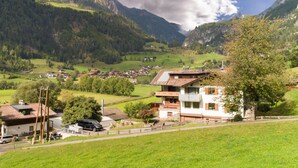 Un village de montagne aux maisons traditionnelles, sous un ciel dégagé, entouré d’une végétation luxuriante.