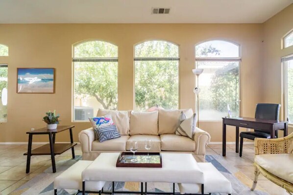 A living room with a beige sofa, a coffee table with a tray, a small table with a plant, and a chair.