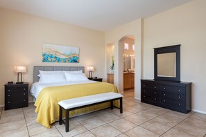A bedroom with a bed, bedside tables, a bench, a dresser, a mirror, and a painting on the wall.