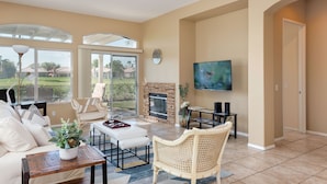 A spacious living room with a fireplace, comfortable seating, a flat-screen TV, and large windows offering a view of the outdoors. - Private home,2 King Beds, near Empire Polo, Tennis, Pools, Coachella, Horse Pk, (Indio)
