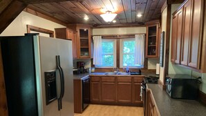 Eine Küche mit Holzausstattung, einem Kühlschrank, einer Spüle und einem Fenster mit Vorhängen.