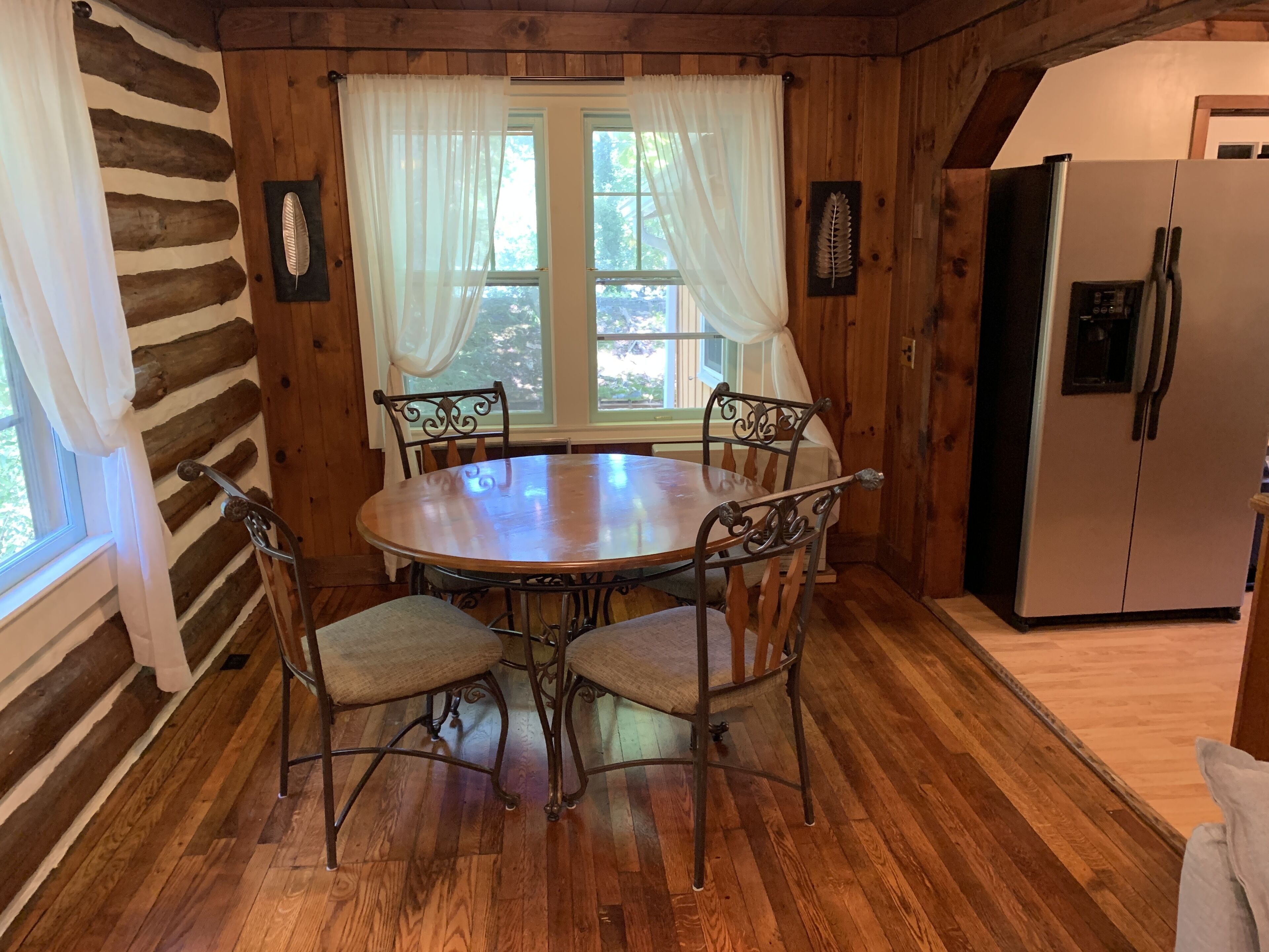 L’intérieur d’un chalet en bois comprend une table de salle à manger ronde entourée de quatre chaises, un réfrigérateur et une fenêtre avec des rideaux.