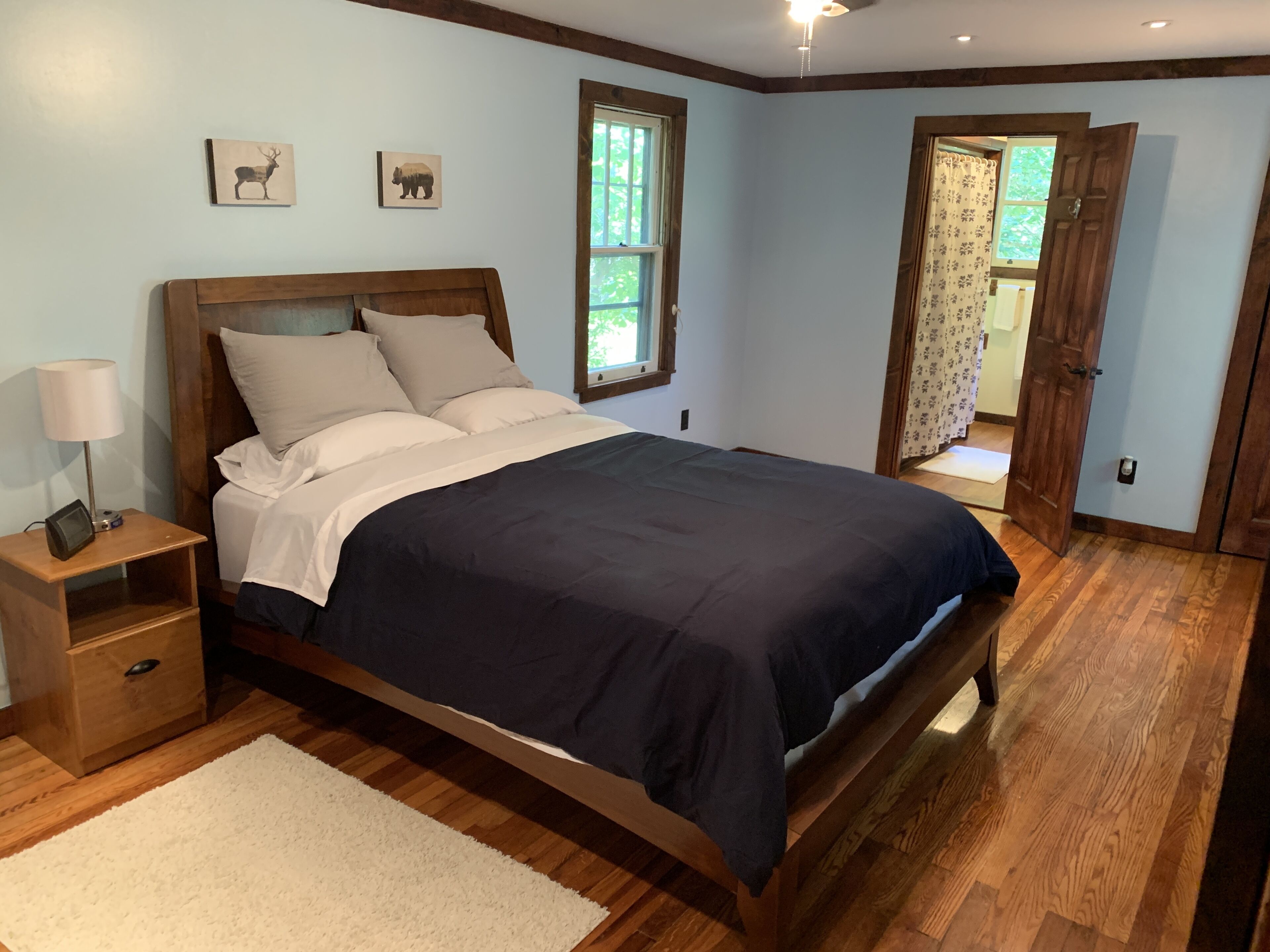 Un dormitorio con cama de madera, mesita de noche, lámpara y ventana con vista a la vegetación.