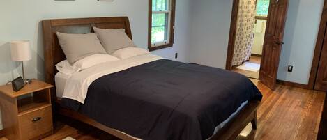 Un dormitorio con cama de madera, mesita de noche, lámpara y ventana con vista a la vegetación.