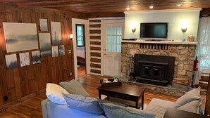 Ein gemütliches Wohnzimmer mit Kamin aus Stein, Holzwänden und einem darüber montierten Fernseher.