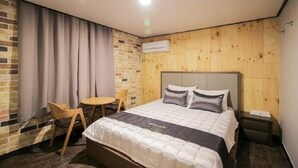 A hotel room with a bed, a small table, a chair, and a wooden wall. - Hotel The May (Busan)