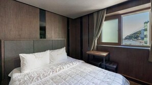 A hotel room with a large bed, a small table, and a window with a view of a bridge. - Hotel The May (Busan)