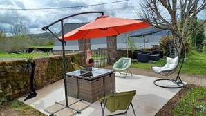 An outdoor patio with a wicker table, a hanging chair, a swing chair, and a red umbrella providing shade. - House in Carladez with private sauna (Brommat)