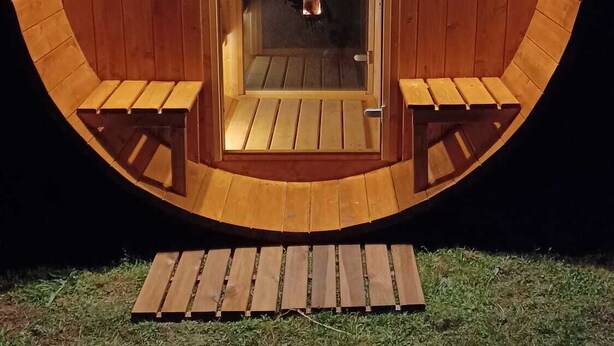 A circular wooden structure with a door, two benches, and a fire visible inside. - House in Carladez with private sauna (Brommat)