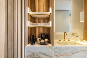 A modern bathroom with a marble countertop, a coffee maker, a kettle, and a sink with gold faucets. - Avgoustos Suites - Adults only (Naxos)