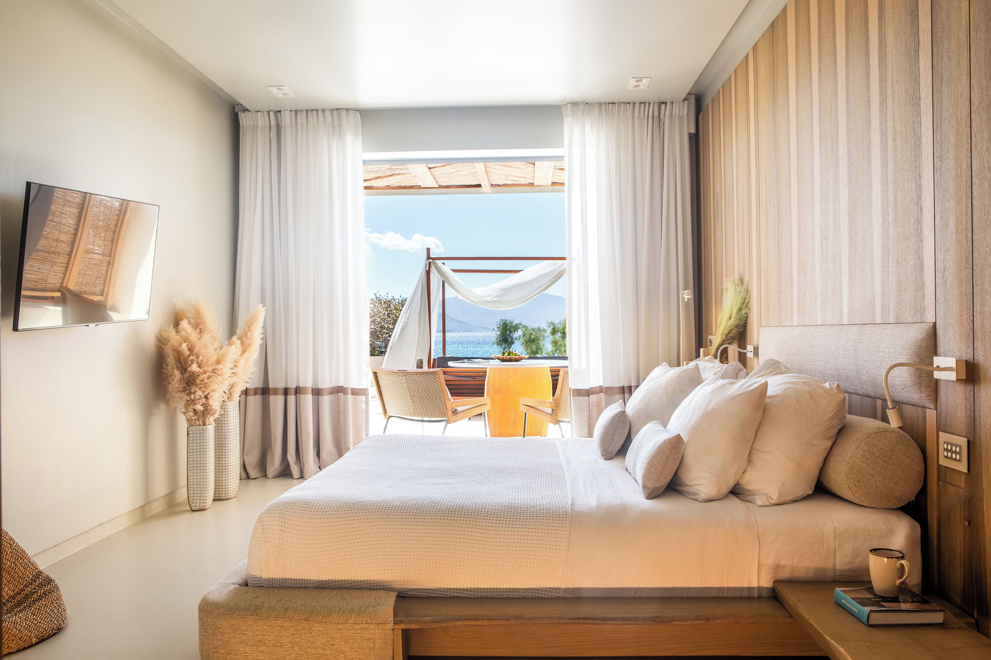 Un dormitorio con una cama grande, vistas al exterior, una zona de comedor y un televisor montado en la pared.