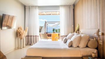 Un dormitorio con una cama grande, vistas al exterior, una zona de comedor y un televisor montado en la pared.