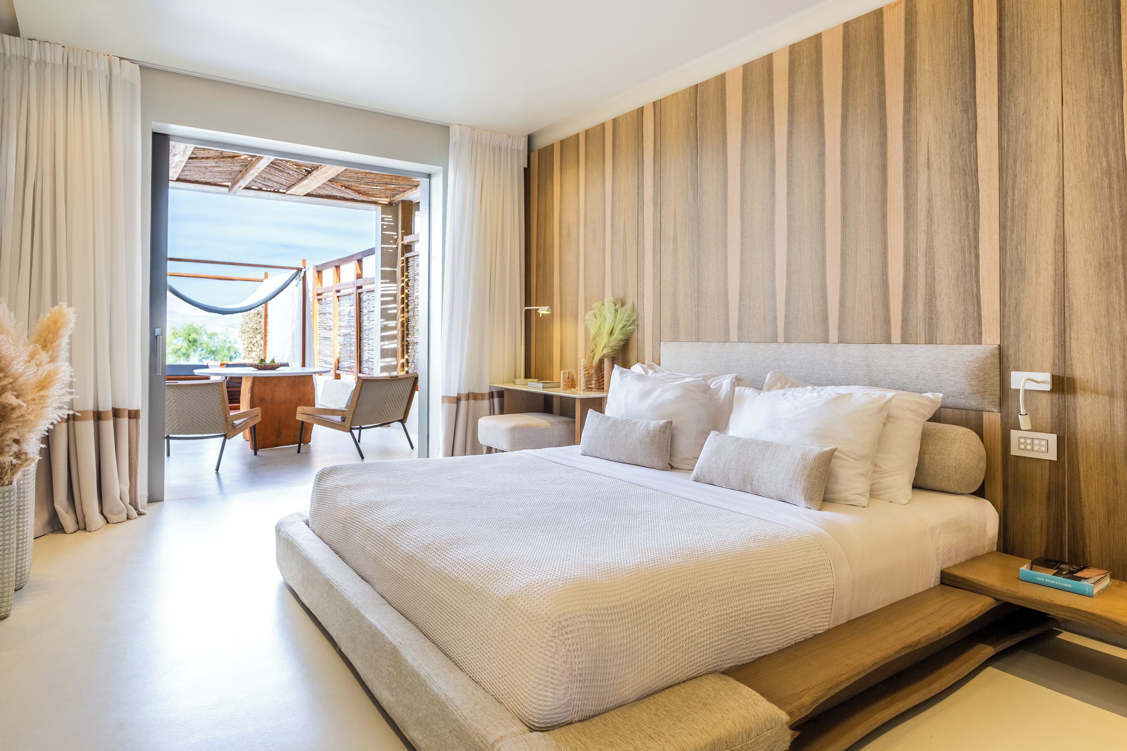 A modern bedroom with a large bed, a wooden accent wall, a desk, and a view of the outdoors.