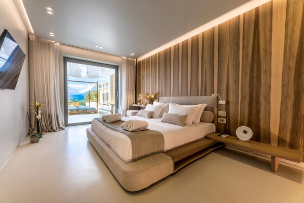 A modern bedroom with a large bed, a bedside table, and a view of the outdoors. - Avgoustos Suites - Adults only (Naxos)