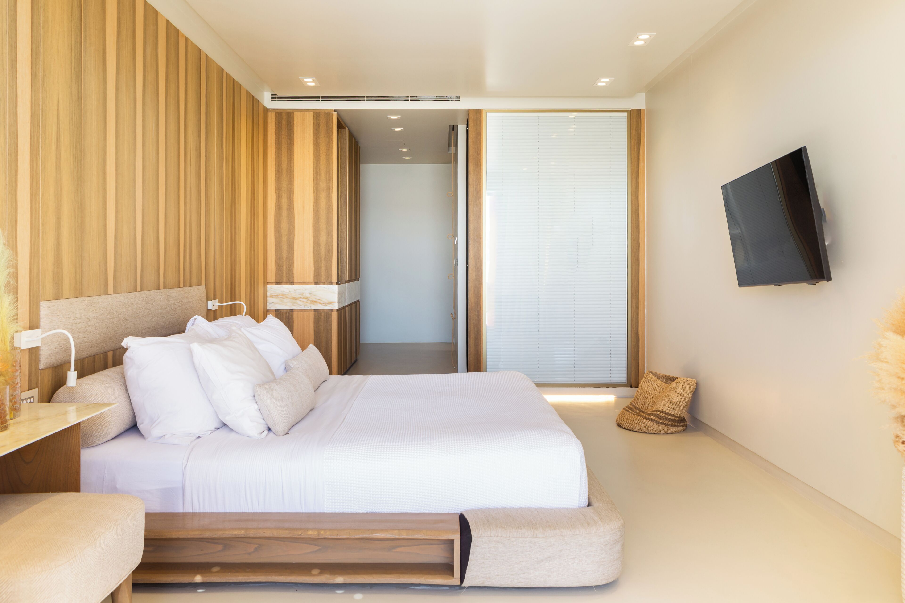 Ein modernes Schlafzimmer mit einem großen Bett, einem Nachttisch, einem an der Wand montierten Fernseher und einer Schiebetür zu einem anderen Raum.