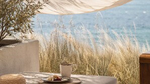 A table with a plate of food, a mug, and a straw hat under a canopy overlooking the sea. - Avgoustos Suites - Adults only (Naxos)